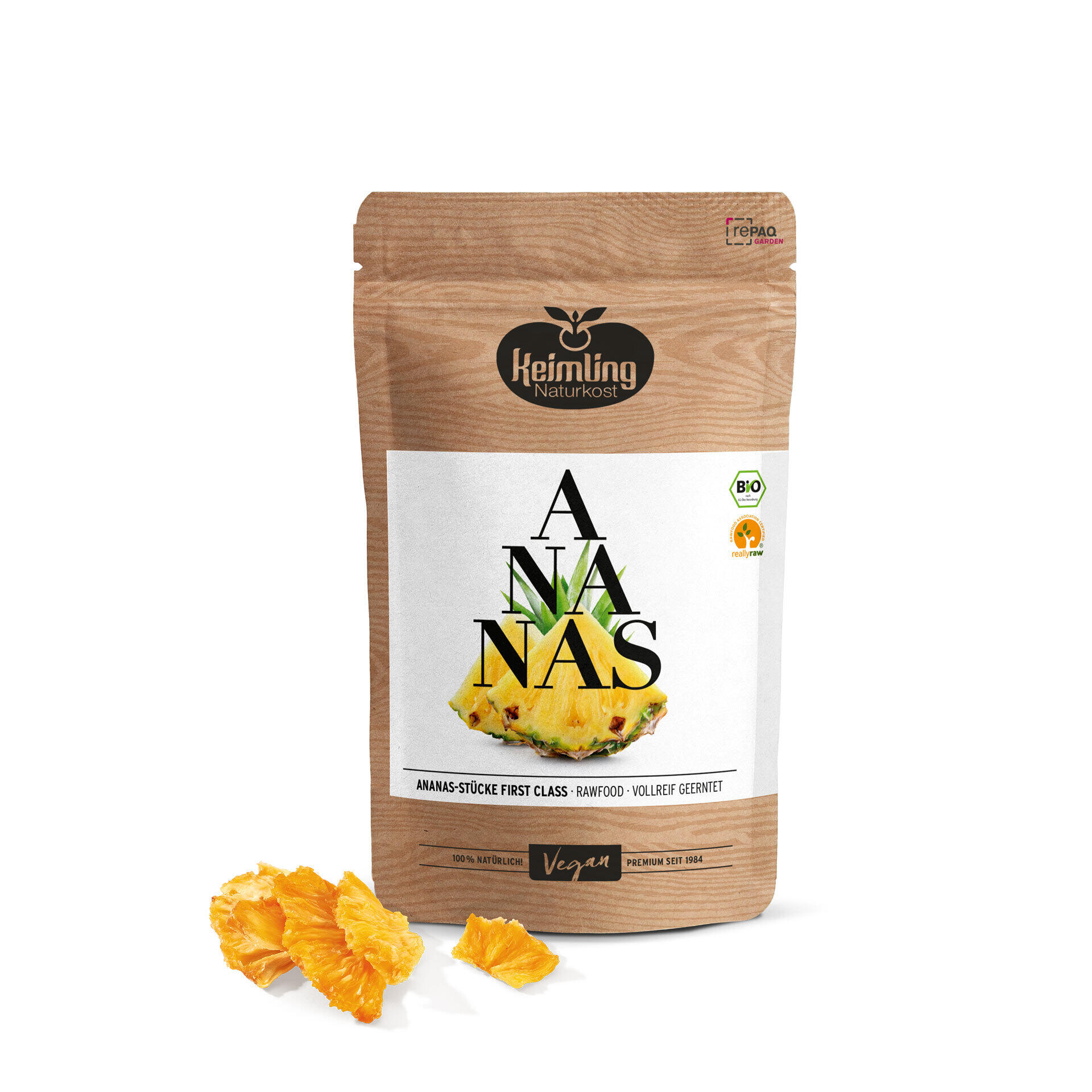 Ananas-Stücke First Class, bio 200 g Verpackung von Keimling Naturkost mit Ananas-Stücken First Class. Vorderseite zeigt eine frische Ananas und die Schrift Ananas. Neben der Verpackung liegen getrocknete Ananasstücke.