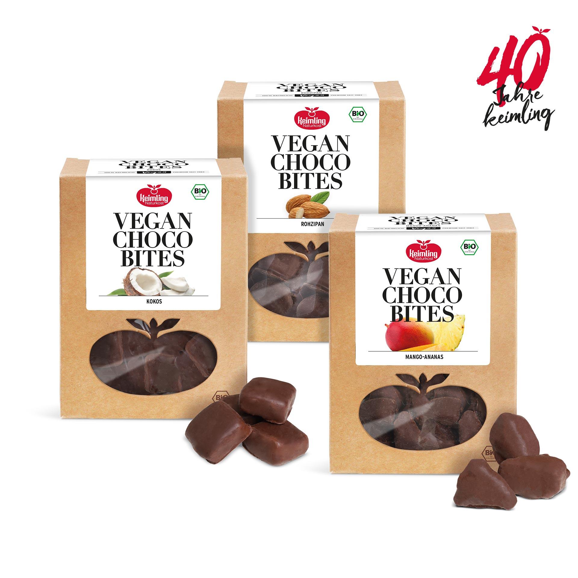 Drei Packungen veganer Bio-Pralinen Keimling Naturkost Vegan Choco Bites in den Sorten Kokos, Rohzipan und Mango-Ananas. Jede Packung zeigt transparente Apfelfenster mit Schokoladenstücken.