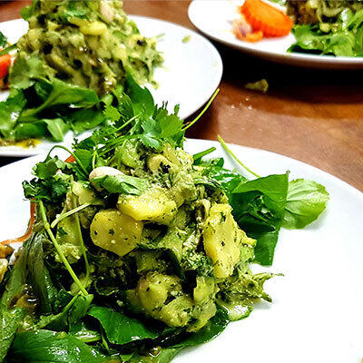 Rohkost-Rezept: Zucchini in Thai Basilikum von Boris Lauser Drei weiße Teller mit einer rohen Zucchini-Mischung in grünem Thai-Basilikum liegen auf einem Holztisch. Das Gemüse wird auf frischem Blattgrün angerichtet.