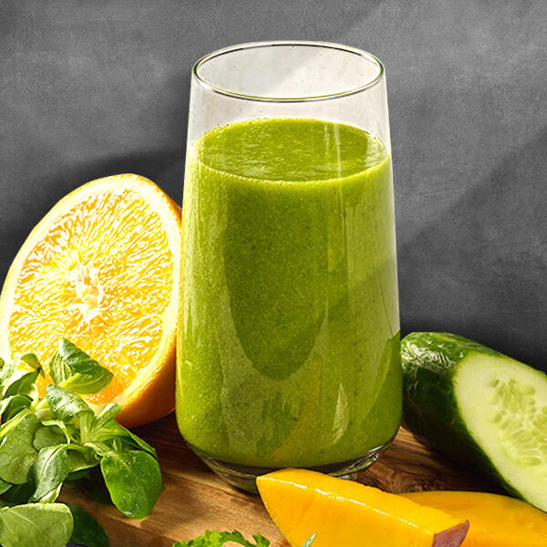 Grüner Smoothie von Peter Dreverhoff Grüner Smoothie in einem Glas steht auf einem Holzbrett. Daneben liegen eine halbierte Orange, ein halber Gurke, Mangostücke und frische grüne Blätter.