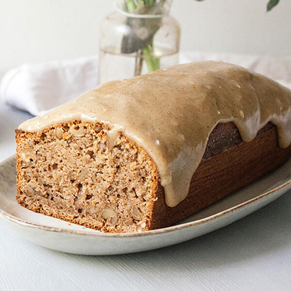 Walnusskuchen mit Walnuss-Frosting Saftiger Walnusskuchen mit sichtbaren Walnussstücken auf einem Teller. Der Kuchen ist mit cremigem, beige-braunem Walnussfrosting überzogen, das leicht über die Seiten läuft.