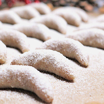 Leckere Rohkost Vanillekipferl Mehrere Rohkost Vanillekipferl liegen nebeneinander auf einer Holzoberfläche. Die Kipferl sind mit Puderzucker bestäubt und haben eine typische Halbmondform.