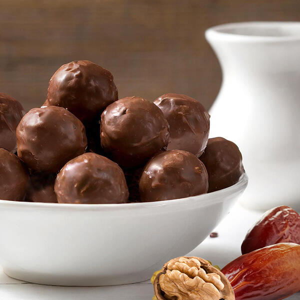 Schokoladige Energy-Balls aus Trester von Peter Dreverhoff Schokoladige Energy Balls liegen in einer weißen Schale. Im Vordergrund sind Walnüsse und Datteln zu sehen. Im Hintergrund steht ein weißer Milchkrug.