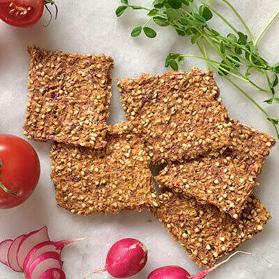 Rohkost Zwiebelbrot von Florian Sauer Vier rechteckige Stücke rohköstliches Zwiebelbrot liegen auf einem hellen Untergrund. Umgeben sind sie von frischen Radieschen, roten Zwiebeln, Tomaten und grünen Kräutern.