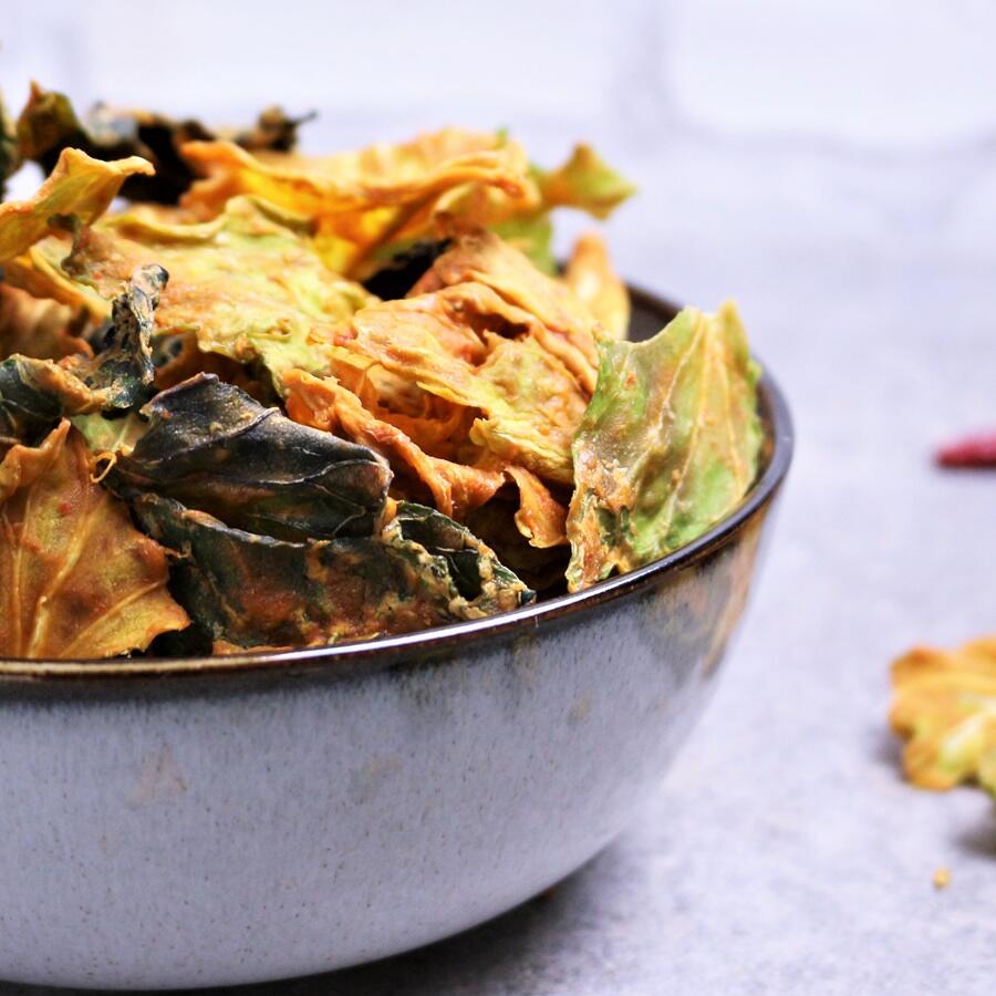 Rohkost-Rezept: Sweet Chili Cream Chips, roh-vegan Eine Schale mit knusprigen, bunten Wirsingchips in den Farben Grün, Gelb und Orange steht auf einer hellen Oberfläche.