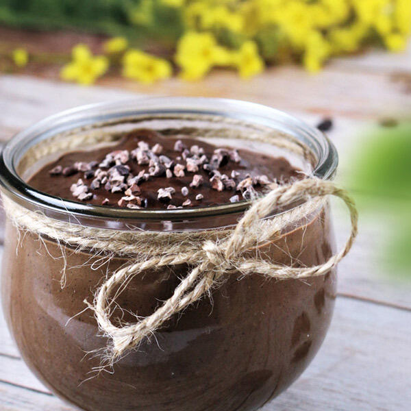 Leckerer Schoko-Sahnepudding mit Schokosplits, roh-vegan Ein Glas mit roh-vegane Schoko-Sahnepudding, dekoriert mit Schokosplits. Das Glas ist mit einer Schnur als Schleife verziert und steht auf einer hellen Holzoberfläche.