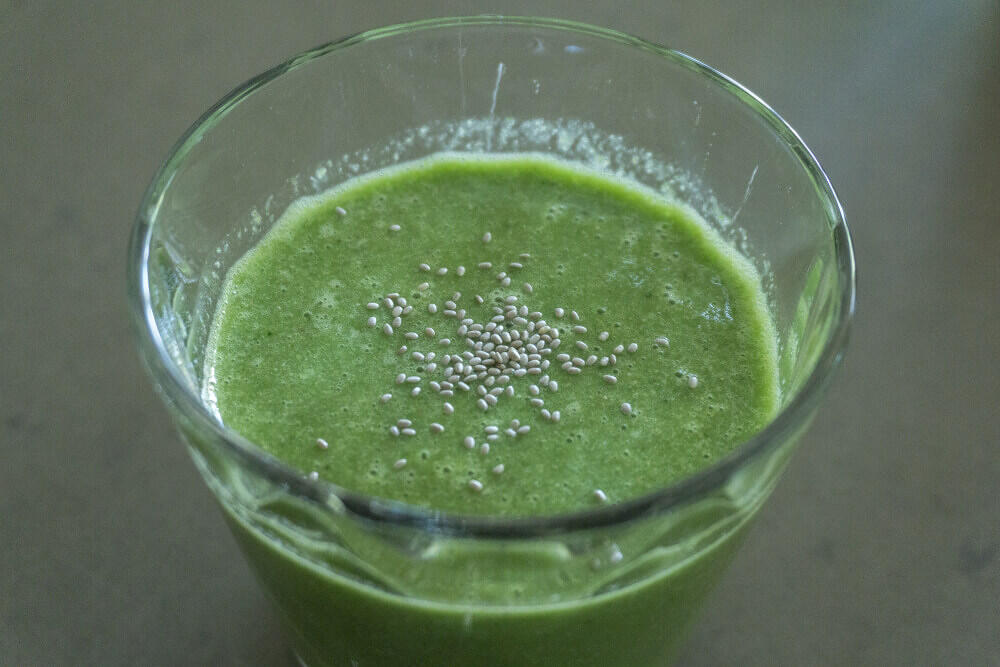 GrĂŒner Smoothie in einem klaren Glas mit weiĂen Chiasamen als Garnitur auf der OberflĂ€che.