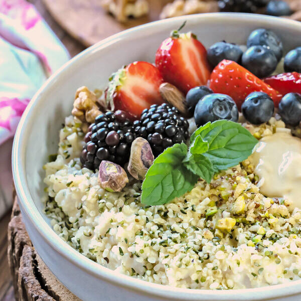 Hirseporridge mit Nüssen, Nussmus und frischen Beeren Schale mit cremigem Hirseporridge, garniert mit frischen Erdbeeren, Brombeeren, Blaubeeren, gehackten Nüssen, Pistazien und einem Minzblatt.