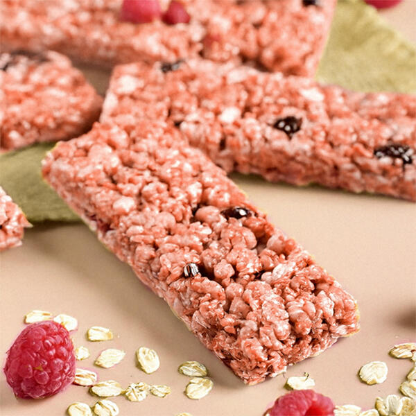 Raw Rasberry Oatbars Vegane Müsliriegel aus Haferflocken, Pekannüssen und Himbeeren liegen auf einer Oberfläche, umgeben von frischen Himbeeren und Haferflocken.