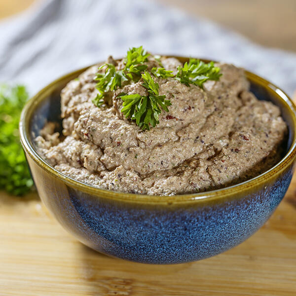 Roh-Vegane Lebervurst von Peter Dreverhoff Schüssel mit roh-veganer Leberwurst, garniert mit frischer Petersilie. Die Leberwurst hat eine cremige, körnige Konsistenz und ist grau-braun.