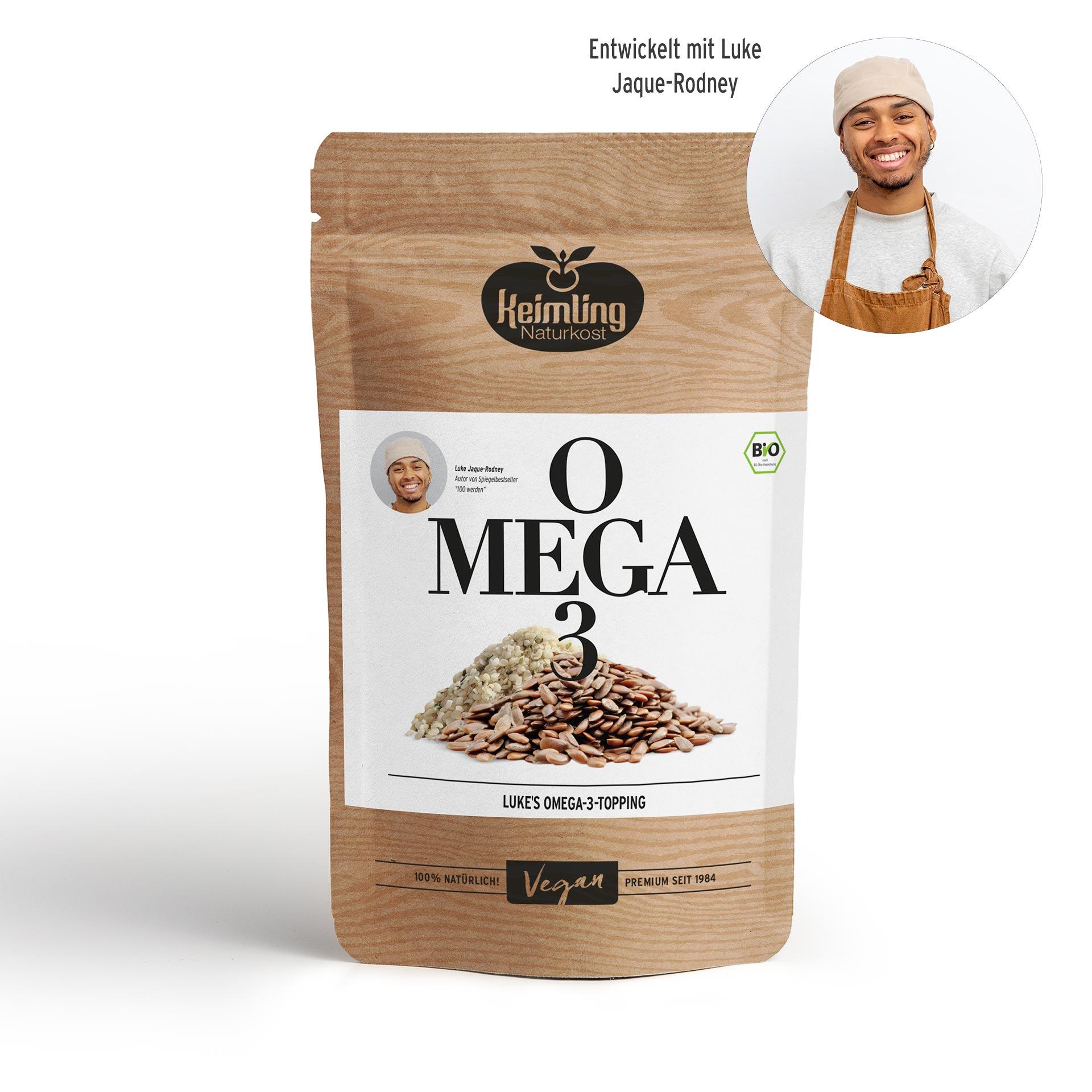 Paket mit Keimling Naturkost Omega 3 Topping, zeigt zwei Sorten Samen, veganes Produkt, 100% natürlich, Bio-Siegel. Porträt von Luke Jaque-Rodney mit weißem Shirt, brauner Schürze und Beanie.