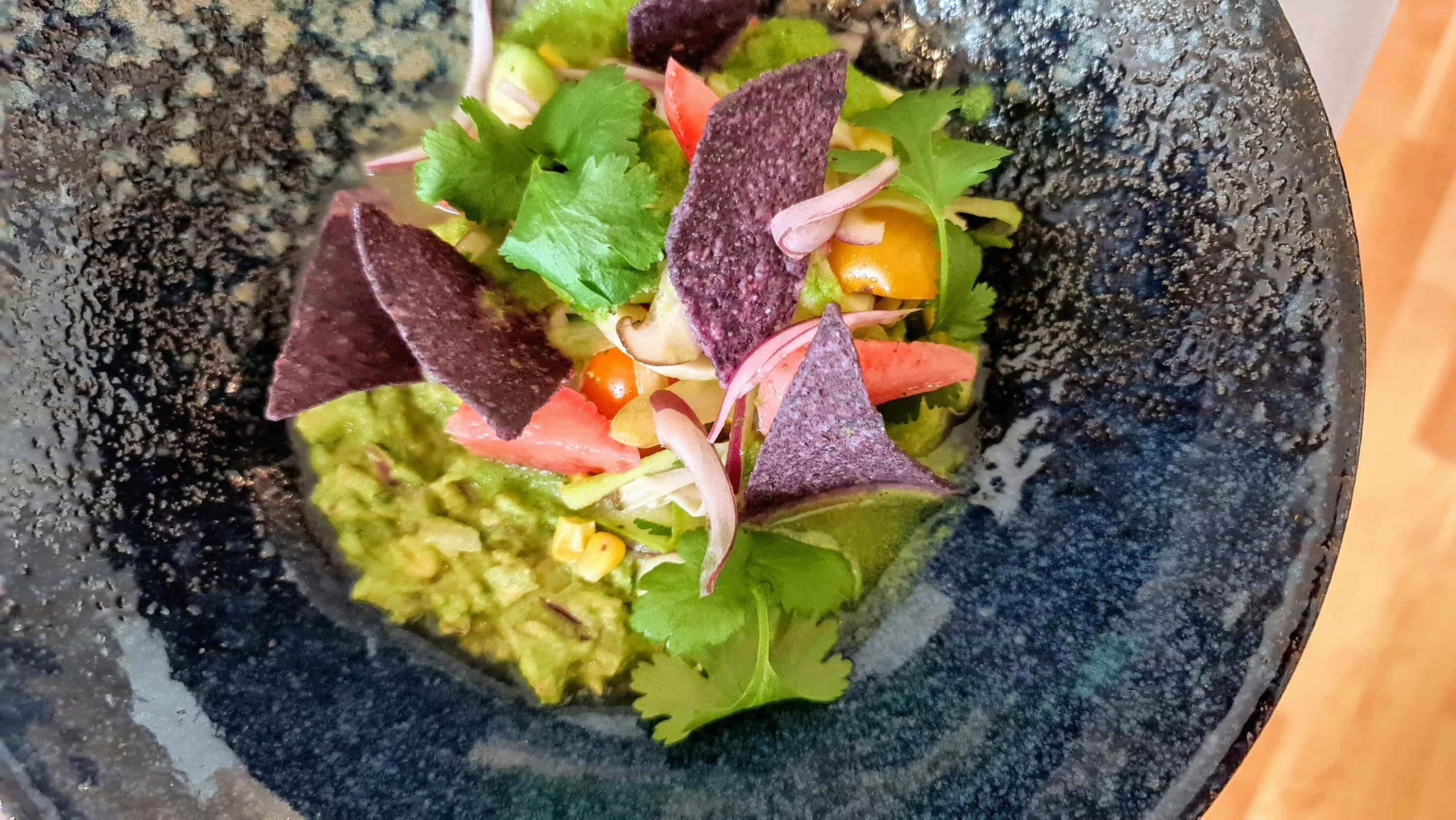 Rohkost-Rezept: Spargel Ceviche von Boris Lauser Dunkelblaue Schale mit Spargel-Ceviche, garniert mit Koriander, roten Zwiebeln, Kirsch- und Cherrytomaten und dunkelvioletten Tortilla-Chips.