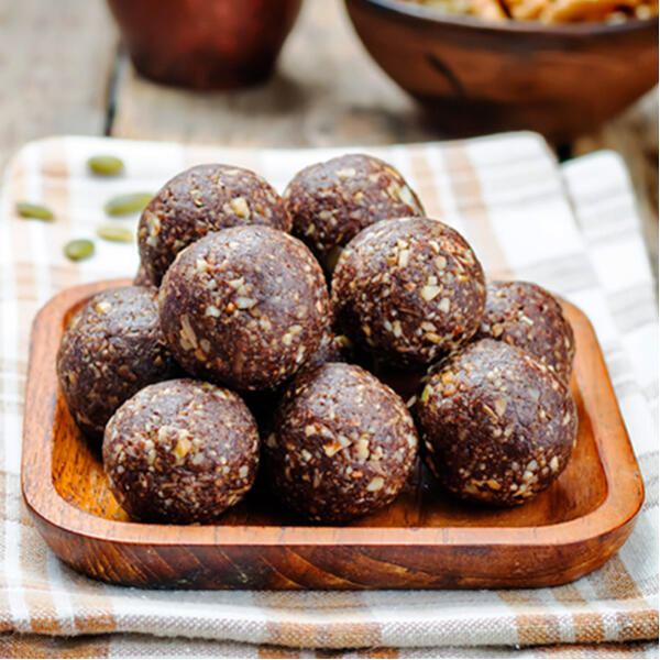 Walnuss Energy Balls  Mehrere runde Walnuss Energy Balls aus Datteln, Haferflocken und Kakao liegen auf einem kleinen, quadratischen Holztablett. Das Tablett steht auf einem karierten Tuch.