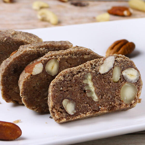 Gemischtes Nussbrot Mehrere Scheiben gemischtes Nussbrot mit sichtbaren Haselnüssen, Pekannüssen und Mandeln liegen auf einem weißen Teller. Die Oberfläche ist grob und nussig strukturiert.