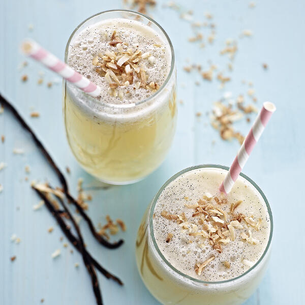 Vanilla de Coco Cocktail Zwei Gläser mit hellgelbem Vanilla de Coco Cocktail haben je einen rosa-weiß gestreiften Trinkhalm. Die Cocktails sind mit Kokosraspeln und Vanilleschoten dekoriert.