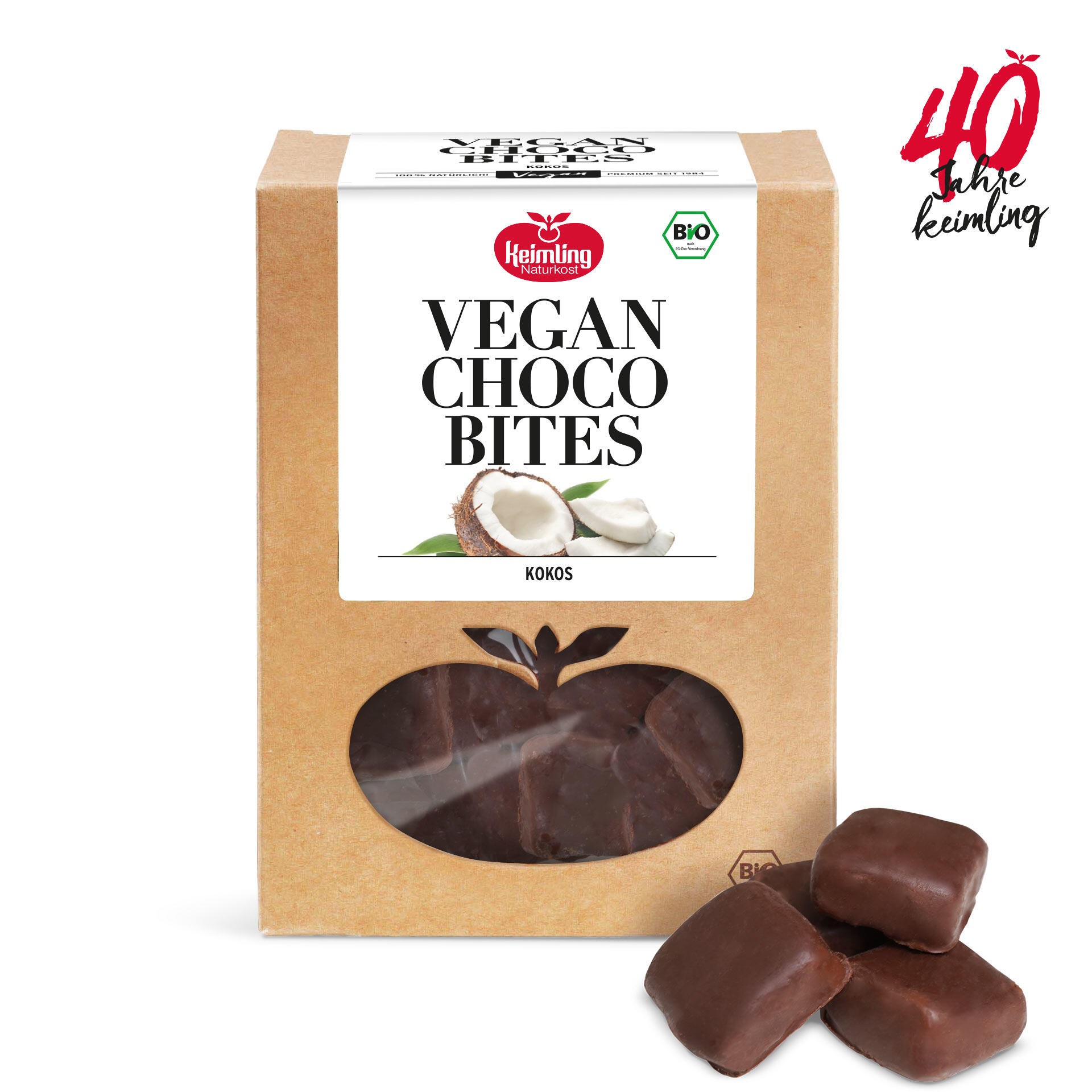 Eine braune Kartonverpackung mit Sichtfenster in Form eines Apfels zeigt vegane Schokoladenstücke. Die Verpackung trägt das Logo Keimling Naturkost und die Bezeichnung VEGAN CHOCO BITES Kokos. Daneben liegen vier einzelne Schokostücke.