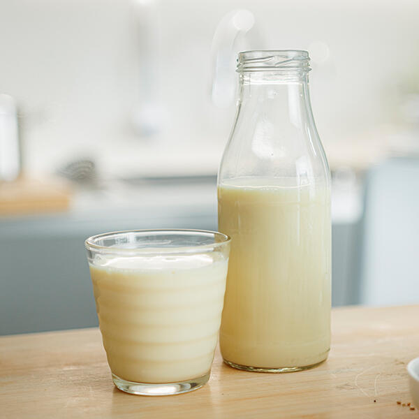 Rohe Hafermilch in 30 Sekunden Glas und Flasche mit roher Hafermilch stehen auf einem Holztisch in einer hellen Küche. Die Flasche ist etwa halb voll.