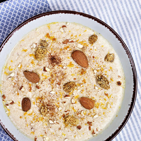 Maulbeeren-Mandel Porridge mit Kokosmilch, roh-vegan Ein Schälchen Maulbeeren-Mandel Porridge mit Kokosmilch zeigt eine cremige Konsistenz, garniert mit ganzen Mandeln, zerhackten Mandeln, getrockneten Maulbeeren und Zimt.