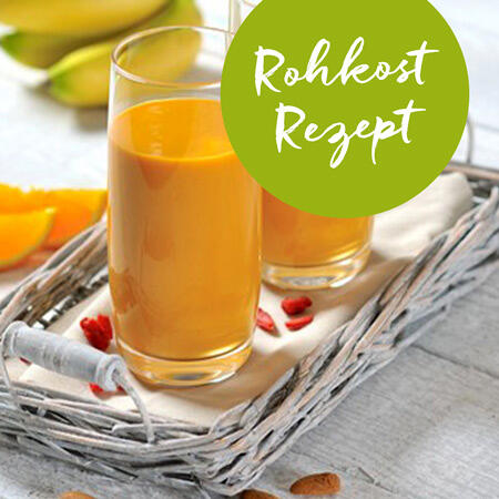 Zwei Gläser mit orangem Rohkost-Saft stehen auf einem weißen Tablett aus geflochtenem Material. Ein grüner Kreis mit weißem Text Rohkost Rezept ist oben rechts zu sehen.