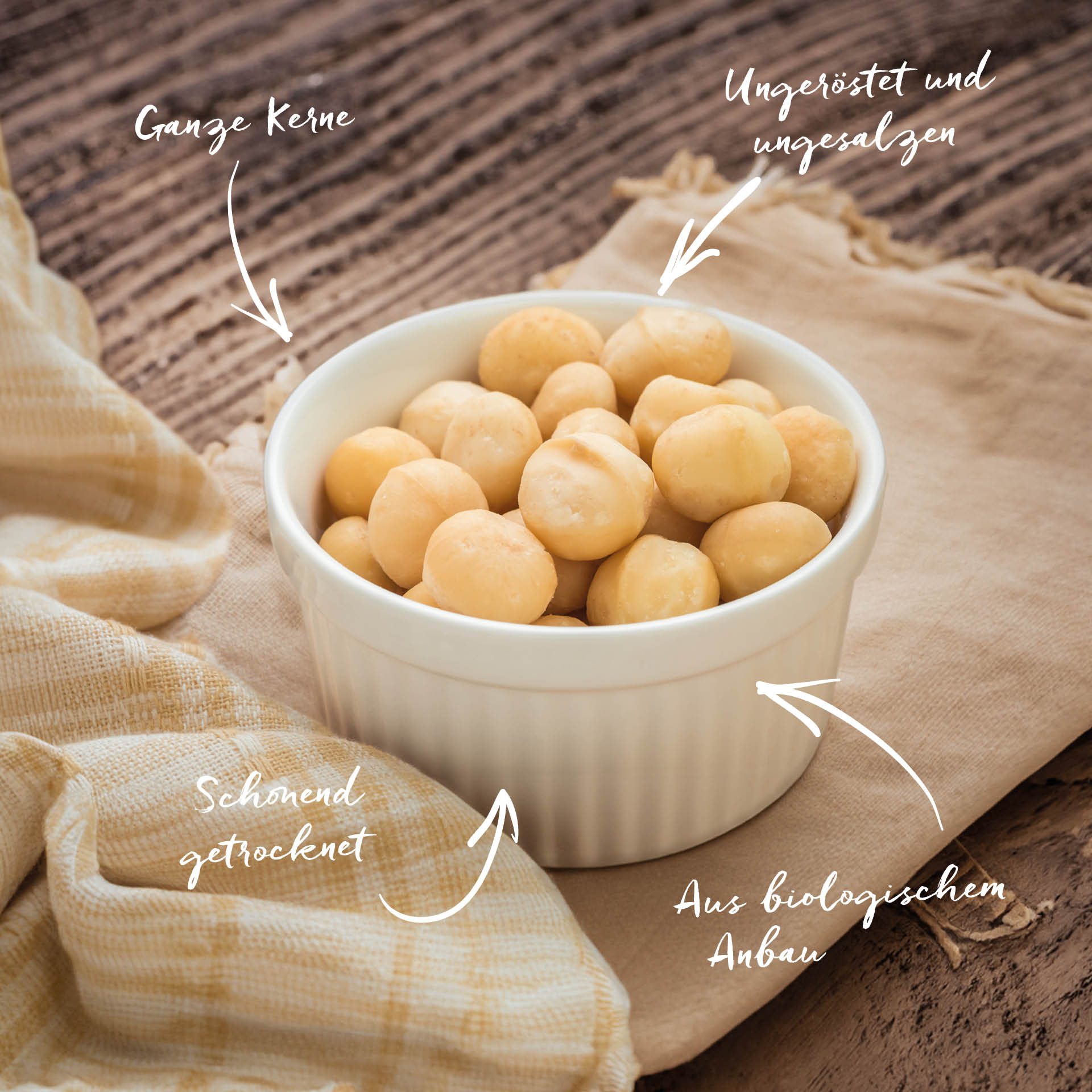 Macadamia, ganze Nüsse, bio 2.5 kg Weiße Schale mit ganzen, ungerösteten und ungesalzenen Macadamianüssen steht auf einem hellen Tuch auf Holzoberfläche. Text zeigt: Ganze Kerne, Ungeröstet und ungesalzen, Schonend getrocknet, Aus biologischem Anbau.