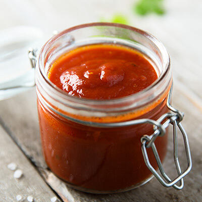 Rohkost-Rezept: Tomaten-Cashew-Aufstrich von Peter Dreverhoff Ein Glas mit rotem, cremigem Tomaten-Cashew-Aufstrich steht auf einem hellen Holztisch. Der Aufstrich wirkt frisch und sämig.
