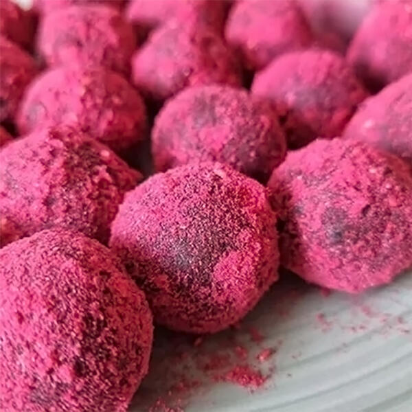 Rohkost Fruchtbällchen von Alexandra Skirde Mehrere pinke Fruchtbällchen mit einer feinen Pulverschicht sind dicht nebeneinander auf einer weißen Oberfläche angeordnet.