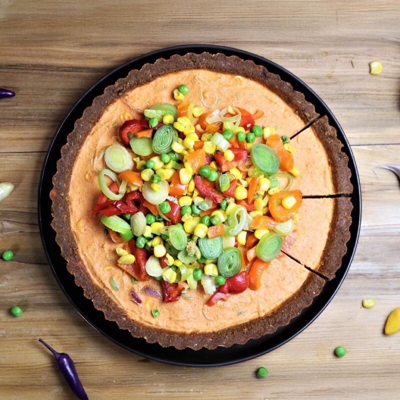 Pikante Mexikanische Gemüse Tarte Pikante mexikanische Gemüsetarte mit einem herb-würzigen dunklen Teigboden. Die Füllung besteht aus einer orangenen Creme und ist mit geschnittenem Lauch, grünen Erbsen, Mais und bunten Paprikastücken belegt. Drei Tortenstücke sind angeschnitten.