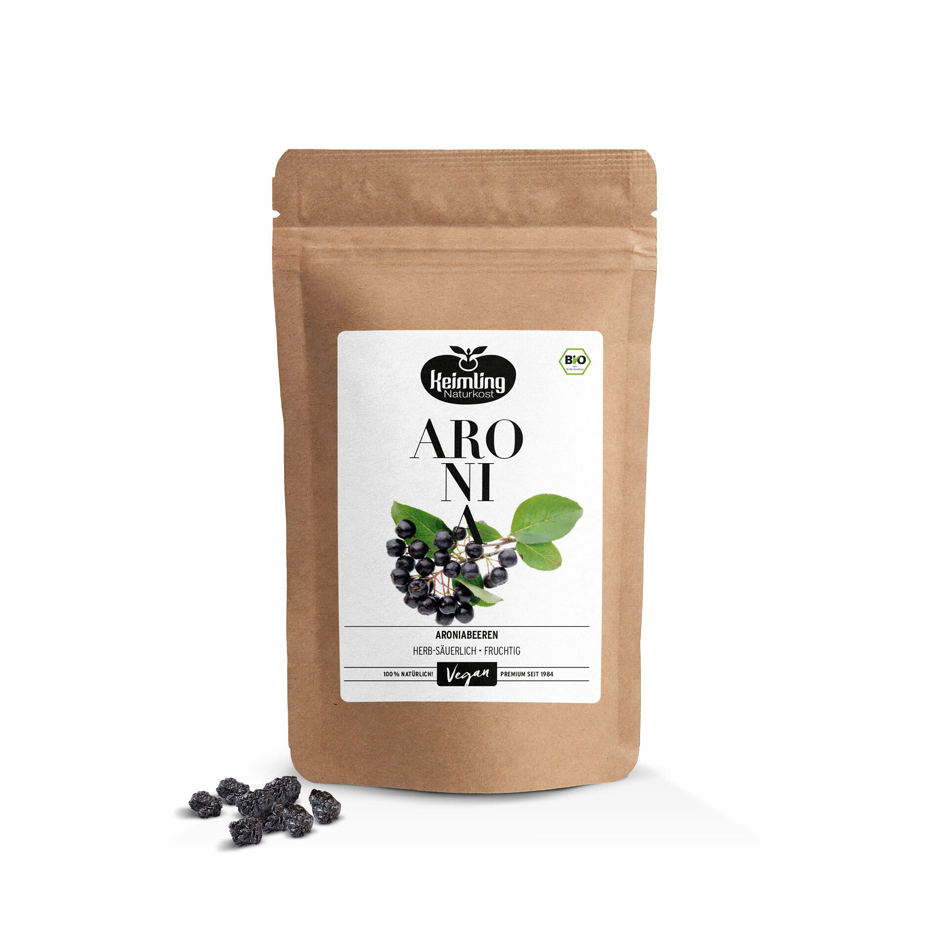 Braune Verpackung mit weißem Etikett zeigt Aroniabeeren und Blätter. Text darauf: Keimling Naturkost, Aronia, Aroniabeeren herb-säuerlich-fruchtig, 100 % natürlich, Vegan, Premium seit 1984. Getrocknete Aroniabeeren liegen links daneben.
