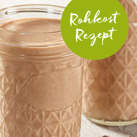Zwei Gläser mit cremigem, braunem Rohkost-Smoothie stehen nebeneinander. Ein grüner Kreis zeigt den Text Rohkost Rezept.