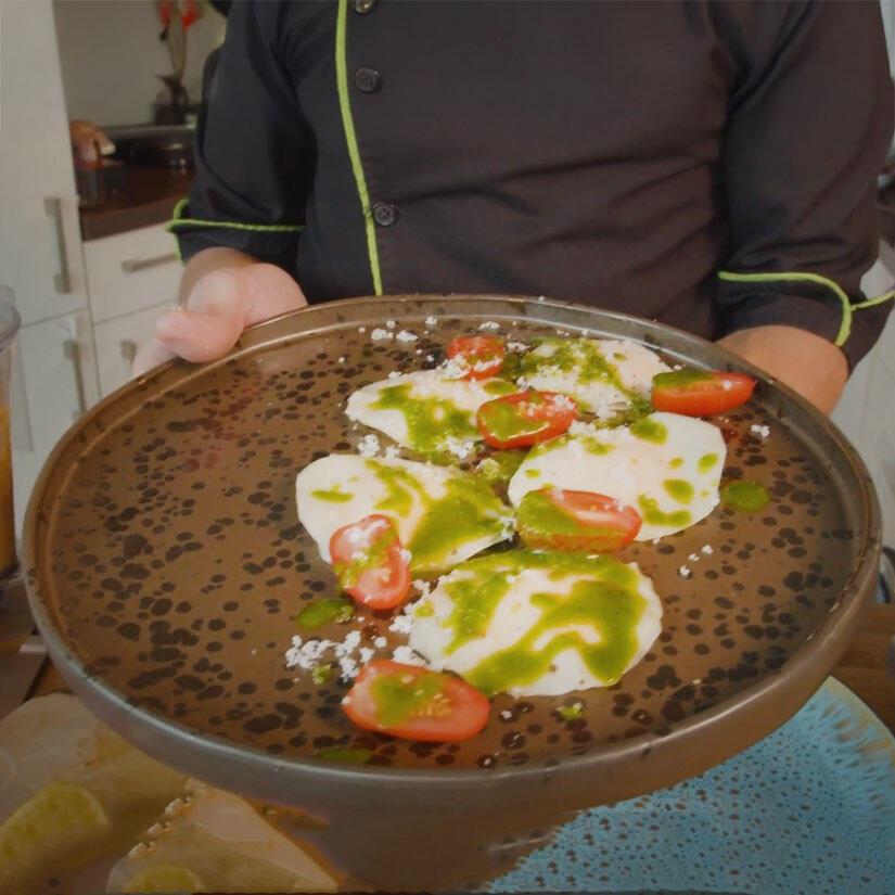 Kohlrabi-Ravioli von Boris Lauser Eine Person hält einen Teller mit Kohlrabi-Ravioli. Die Ravioli sind mit grünem Kräuteröl beträufelt und mit halbierten Cherrytomaten garniert.