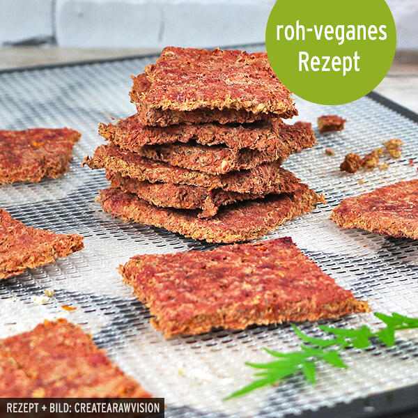 Gemüsetresterbrot, roh-vegan Mehrere quadratische, knusprige Gemüsetresterbrotstücke liegen auf einem Metallsieb, ein Stapel davon ist in der Bildmitte aufgeschichtet. Oben rechts steht im grünen Kreis der weiße Text roh-veganes Rezept.