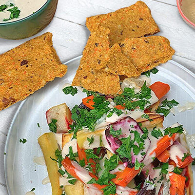 Buntes gebackenes Wurzelgemüse mit Tahinidressing Buntes gebackenes Wurzelgemüse aus Karotten, Pastinaken und roter Bete auf einem Teller mit grün gehackter Petersilie und cremigem Tahinidressing. Daneben liegen mehrere rechteckige, knusprige Cracker.